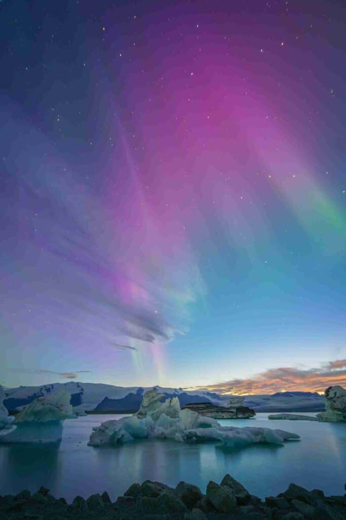 A purple and green northen lights show above and iceberg in Iceland